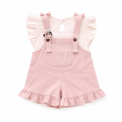 Baby girl wearing a pink striped flutter-sleeve top and blush ruffle shortall with bow details in a soft boutique setting from Lullaby Threads.