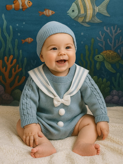 Baby wearing a blue knitted outfit with a sailor collar, sitting against an underwater-themed backdrop.
